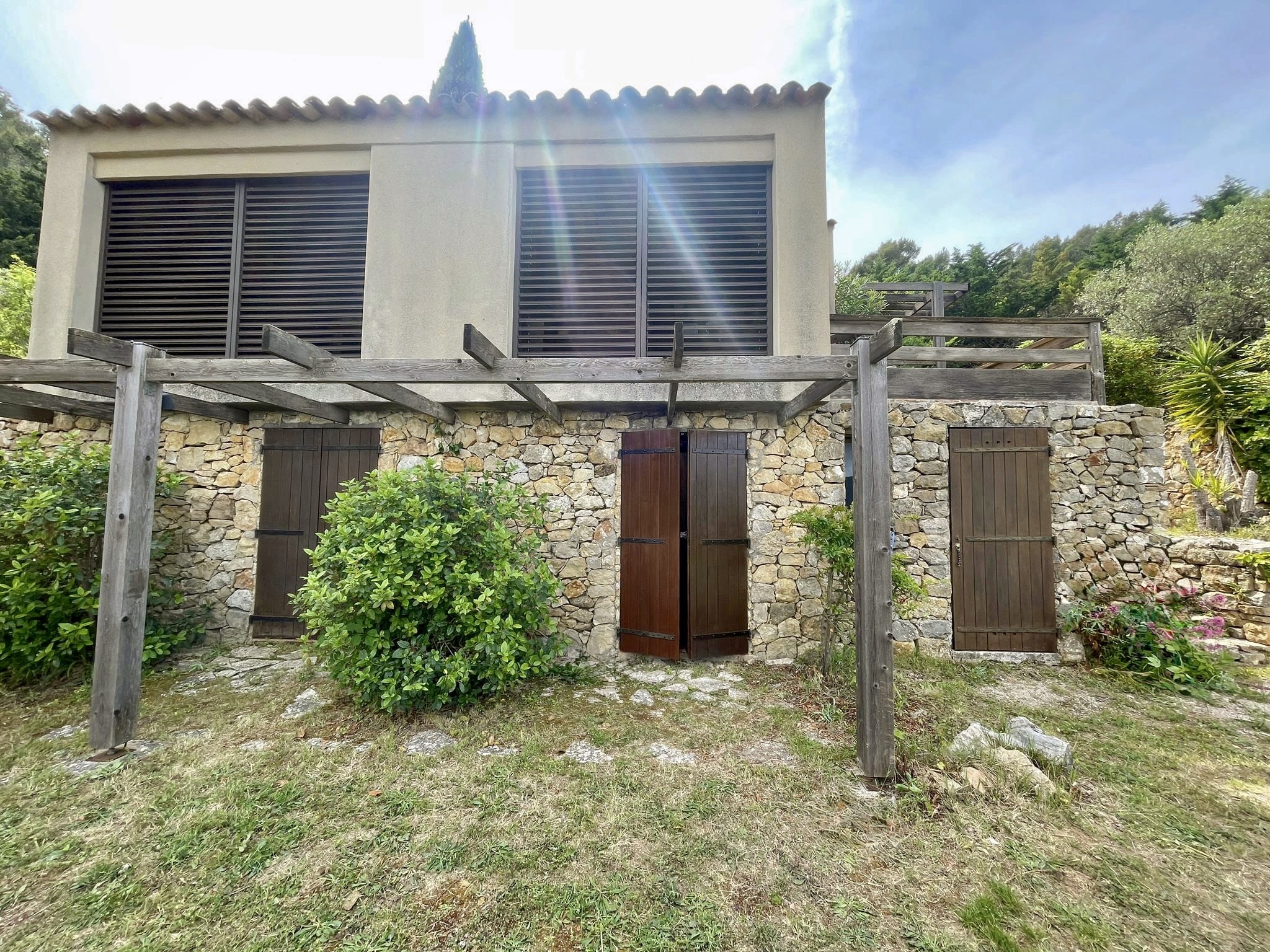 Maison provençale en pierre avec volets bois, pergola rustique et jardin méditerranéen ensoleillé.
