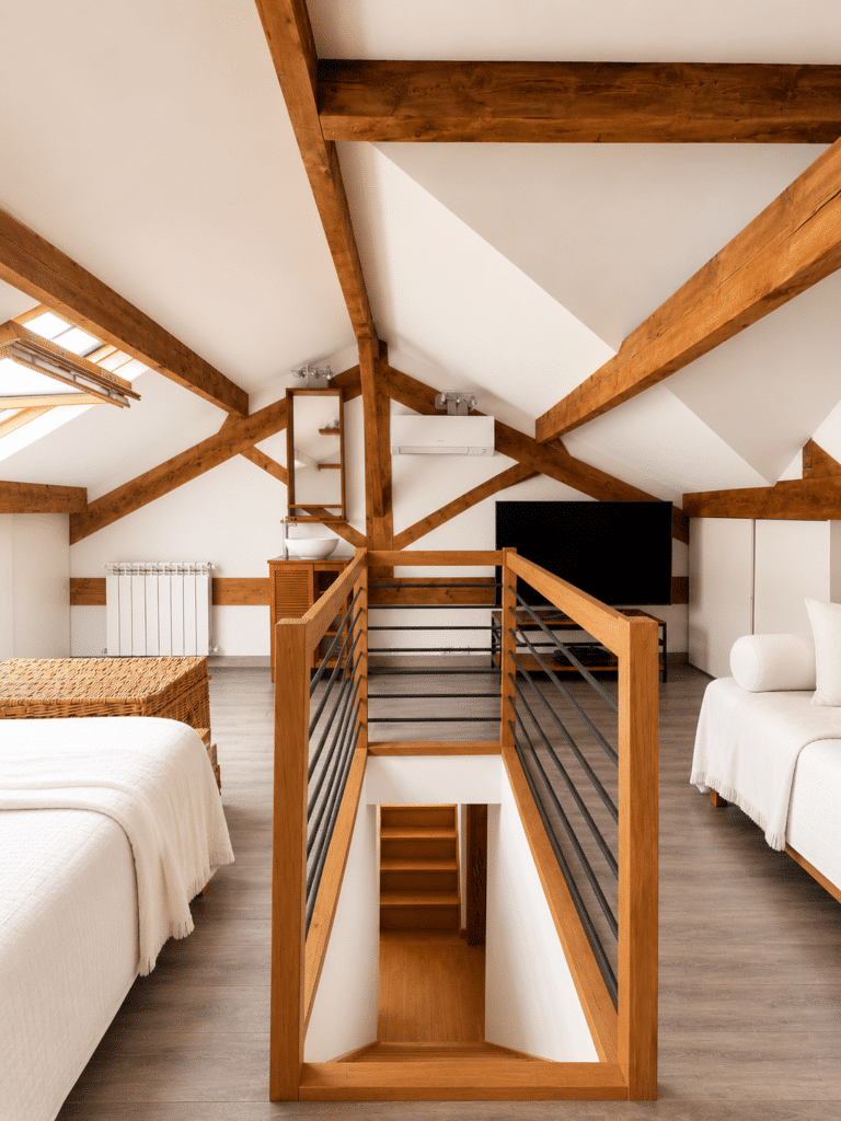 Chambre mansardée lumineuse avec poutres en bois apparentes, escalier central et mobilier blanc épuré.