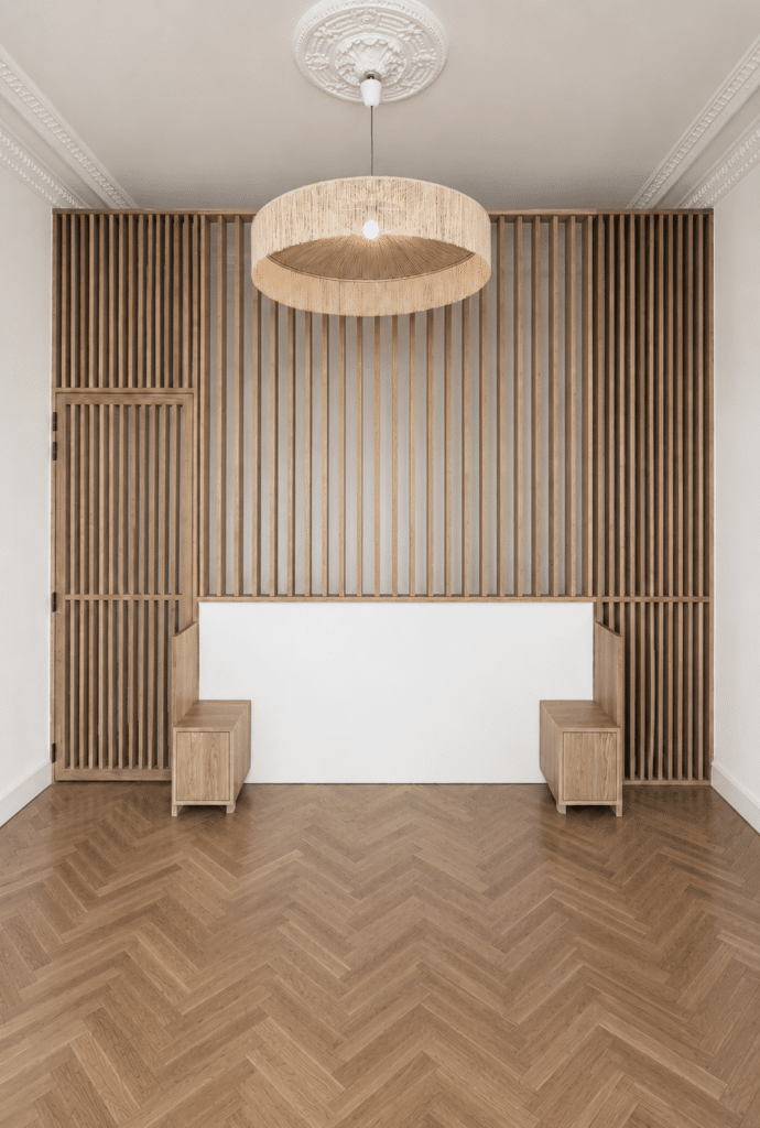 Claustra en bois massif, parquet en chevrons et luminaire en paille dans un intérieur minimaliste élégant.