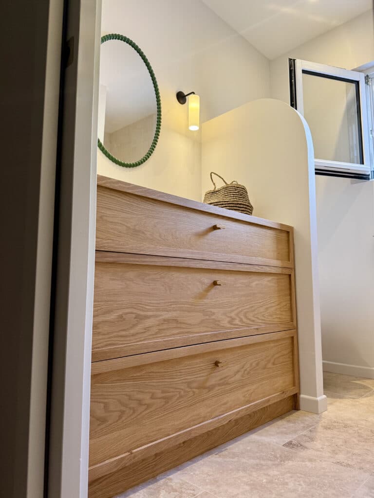 Meuble de salle de bain en chêne, miroir rond à perles vertes et applique moderne dans un intérieur épuré.