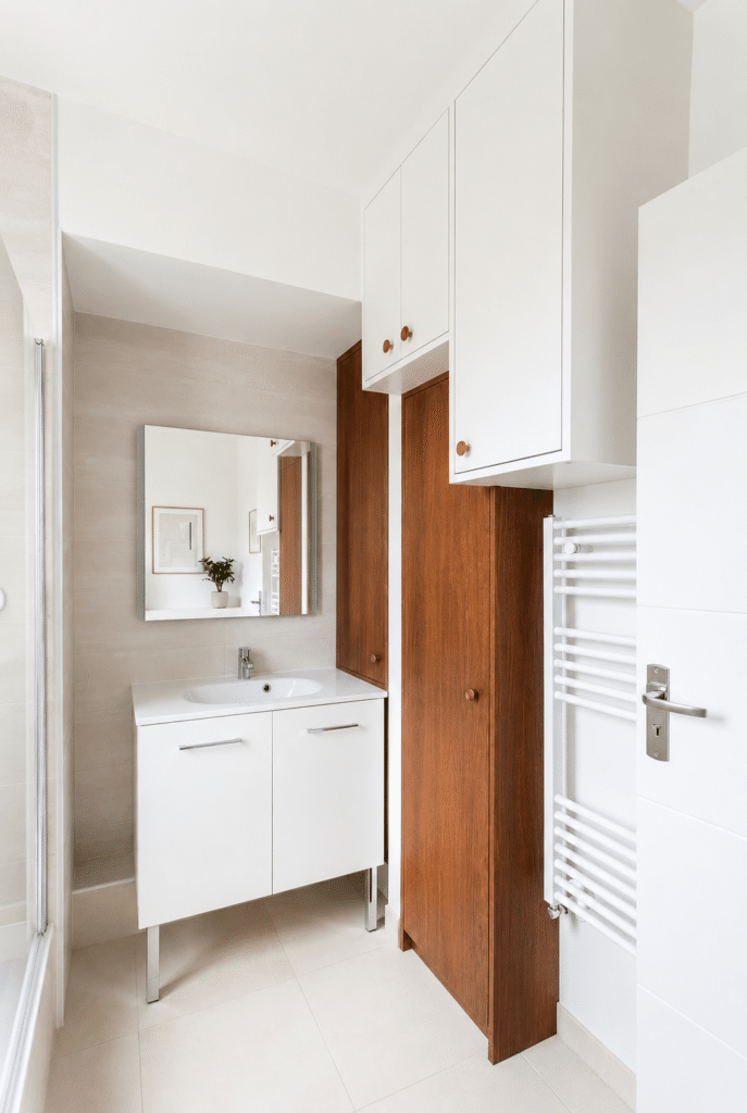 Salle de bain épurée avec meuble blanc, rangements bois, miroir et sèche-serviettes blanc.