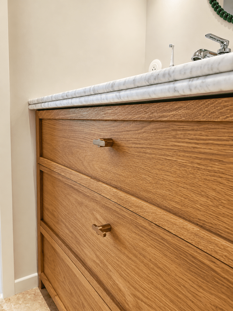Meuble vasque en chêne, plan de travail en marbre et poignées en laiton doré dans une salle de bain moderne.